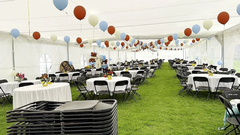Mesas redondas vestidas de blanco bajo la carpa, con globos